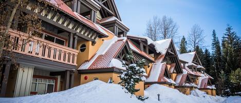 A row of chalet-style buildings with steep roofs and wooden balconies, surrounded by snow.