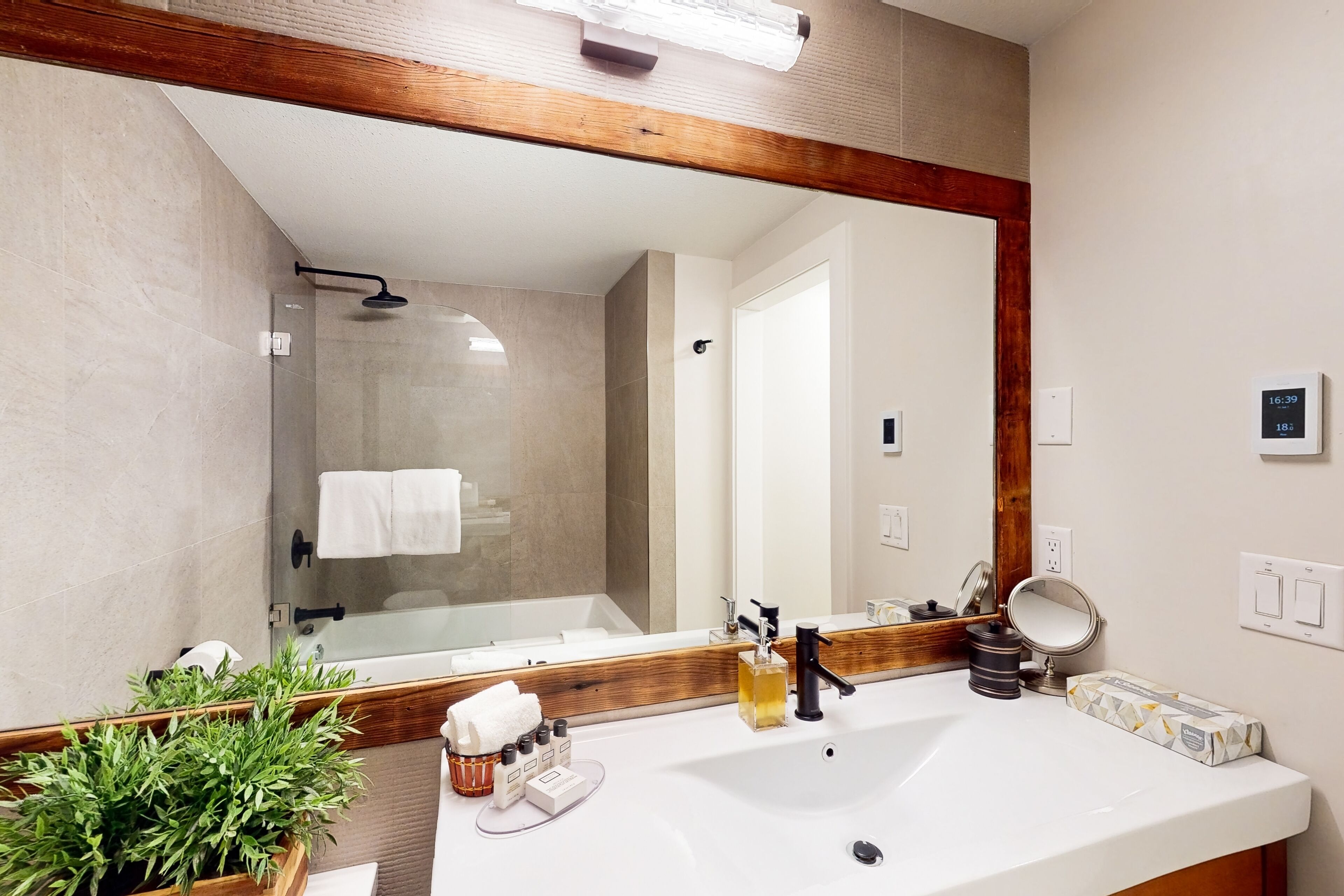 A modern bathroom with a large mirror, white sink, and a shower area.