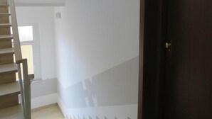 Una escalera con barandilla de madera que lleva a una puerta oscura de madera. Se ve un letrero de salida verde en la pared.