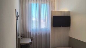 Habitación de hotel con cama, escritorio, silla, televisor montado en la pared y ventana con cortinas.