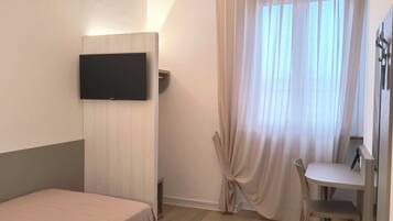 A hotel room with a bed, a desk, a chair, a ceiling fan, and a TV mounted on the wall.