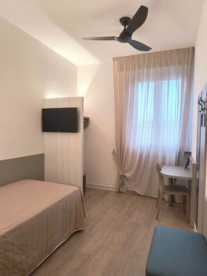 A hotel room with a bed, a desk, a chair, a ceiling fan, and a TV mounted on the wall. - Hotel Marta Forlì (Forlì)