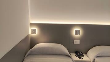 Quarto de hotel com duas camas de solteiro, mesa de cabeceira com telefone e iluminação embutida na parede.