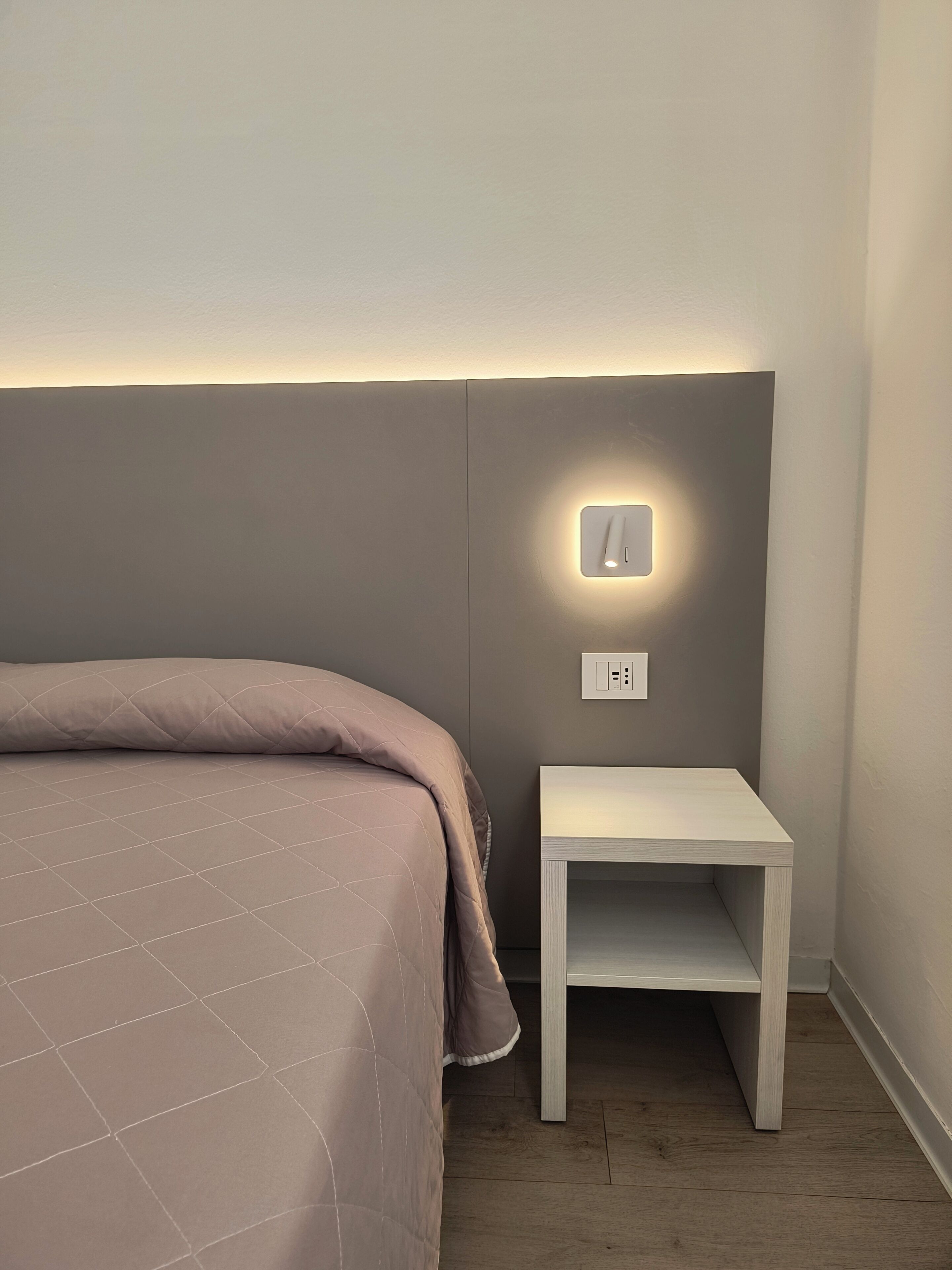 A bedroom with a bed, a bedside table, and a wall-mounted light fixture.
