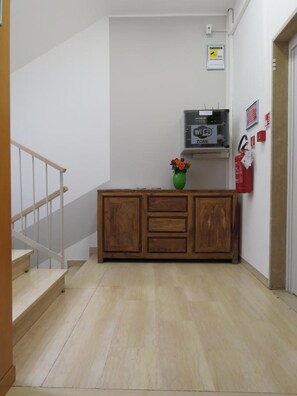 A hallway with a wooden cabinet, a vase with flowers, a Wi-Fi sign, and a fire extinguisher. - Hotel Marta Forlì (Forlì)