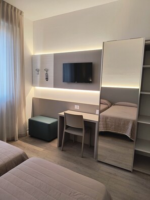 A hotel room with a bed, a desk, a chair, a TV mounted on the wall, and a wardrobe. - Hotel Marta Forlì (Forlì)