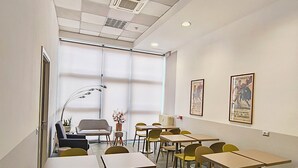 Un salón de conferencias con mesas y sillas, un ventanal grande y un radiador.