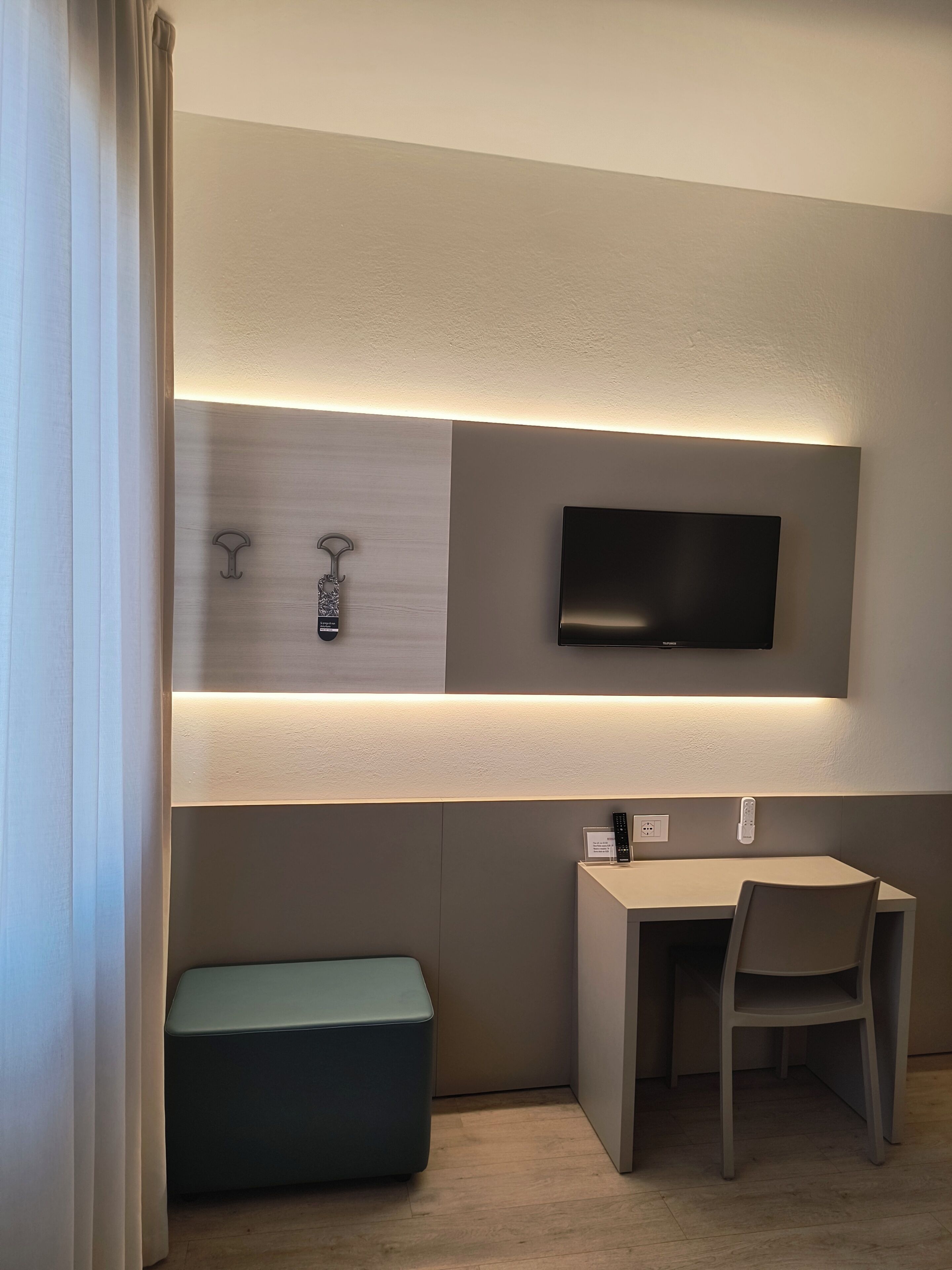 Una habitación moderna con una televisión de pantalla plana montada en la pared, un escritorio con una silla y un banco.