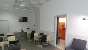 A modern office space with multiple tables and chairs, a reception area, and a television mounted on the wall. - Hotel Marta Forlì (Forlì)