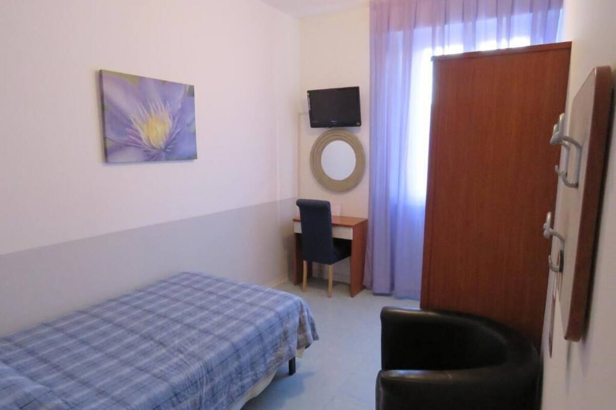 A bedroom with a bed, a desk, a chair, a television, and a door.