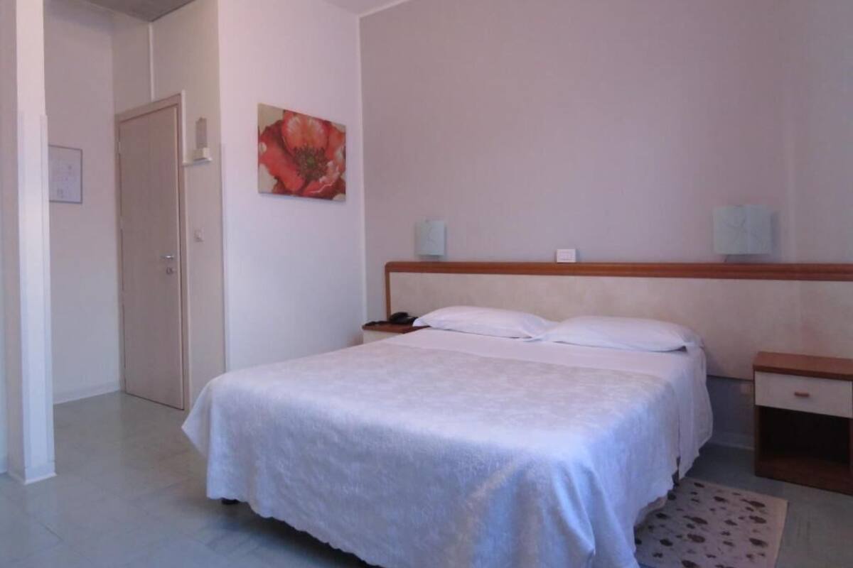 A bedroom with a bed, bedside tables, a nightstand, a door, and a wall-mounted artwork.