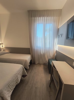 A hotel room with two beds, a desk, and a large window with sheer curtains. - Hotel Marta Forlì (Forlì)
