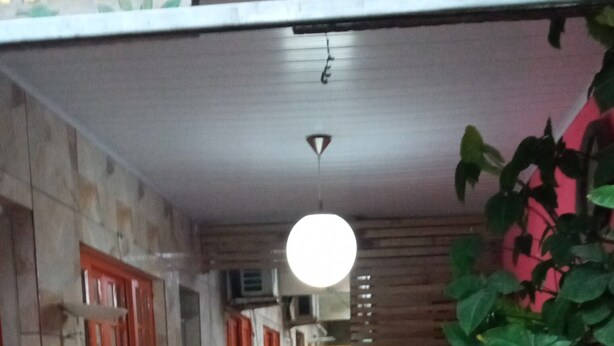 Un couloir étroit au sol carrelé, avec une porte rouge et une plante sur le côté droit.