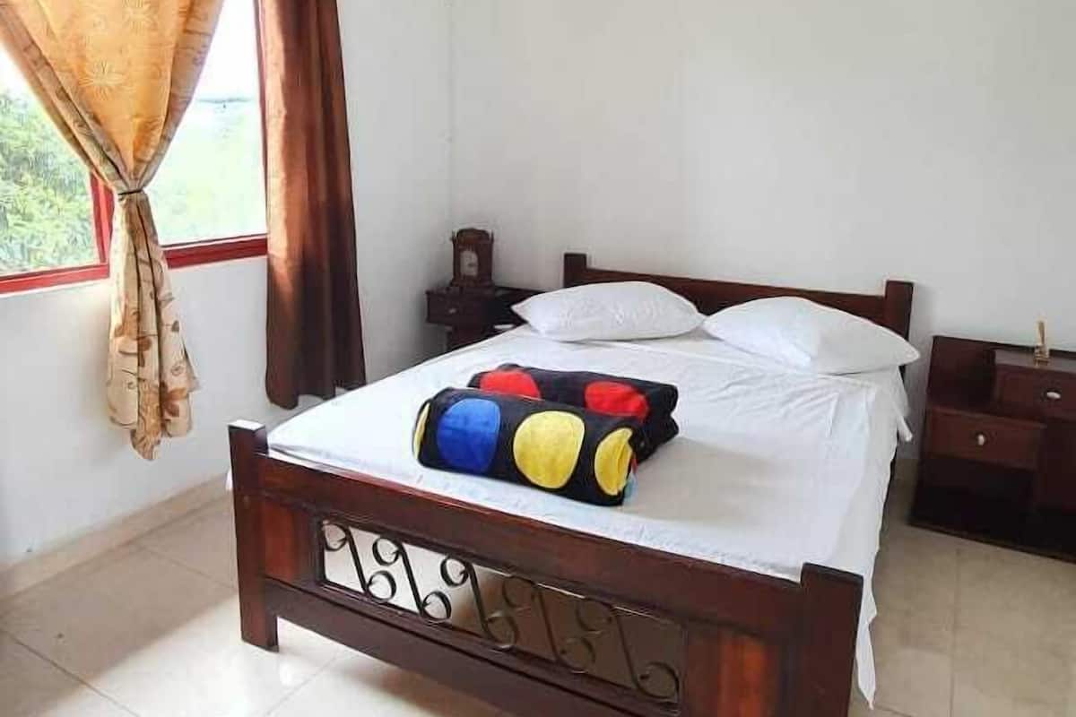 Un dormitorio con una cama de madera, ropa de cama blanca y una almohada colorida.