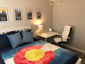 A bedroom with a bed, a desk, a chair, and wall art.