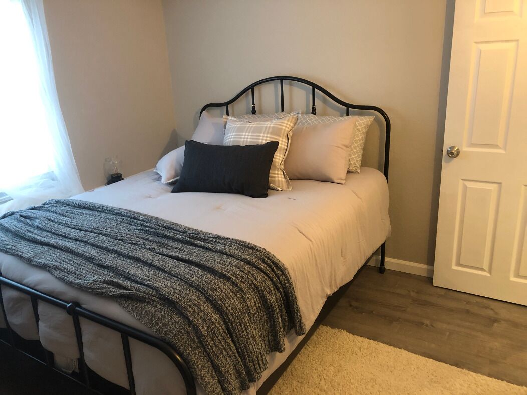 A neatly made bed with a black metal frame, white bedding, and a gray knitted throw.