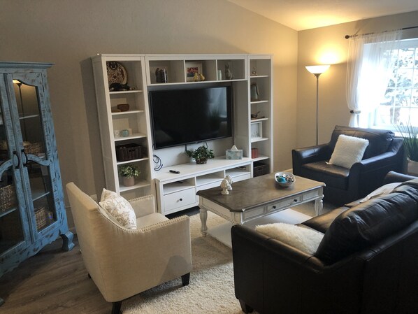 Una sala de estar con televisor, dos sofás, una mesa de centro y un mueble con estantes.