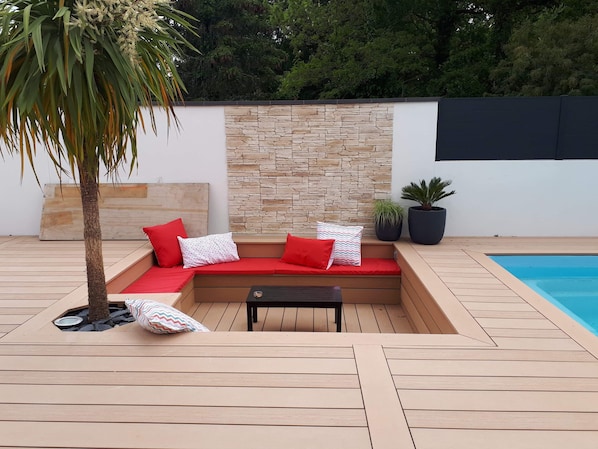 A modern outdoor seating area with a stone wall backdrop, a pool, and potted plants. - Contemporary villa with heated pool (Saint-Sulpice-de-Royan)