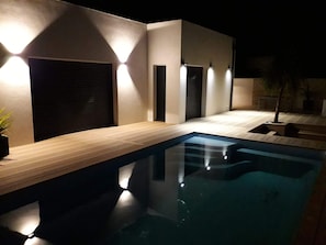 A modern outdoor pool area with a wooden deck, a swimming pool, and a series of wall-mounted lights. - Contemporary villa with heated pool (Saint-Sulpice-de-Royan)