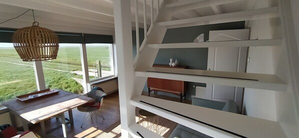 A modern interior with a dining area, a staircase, and a view of a green field.