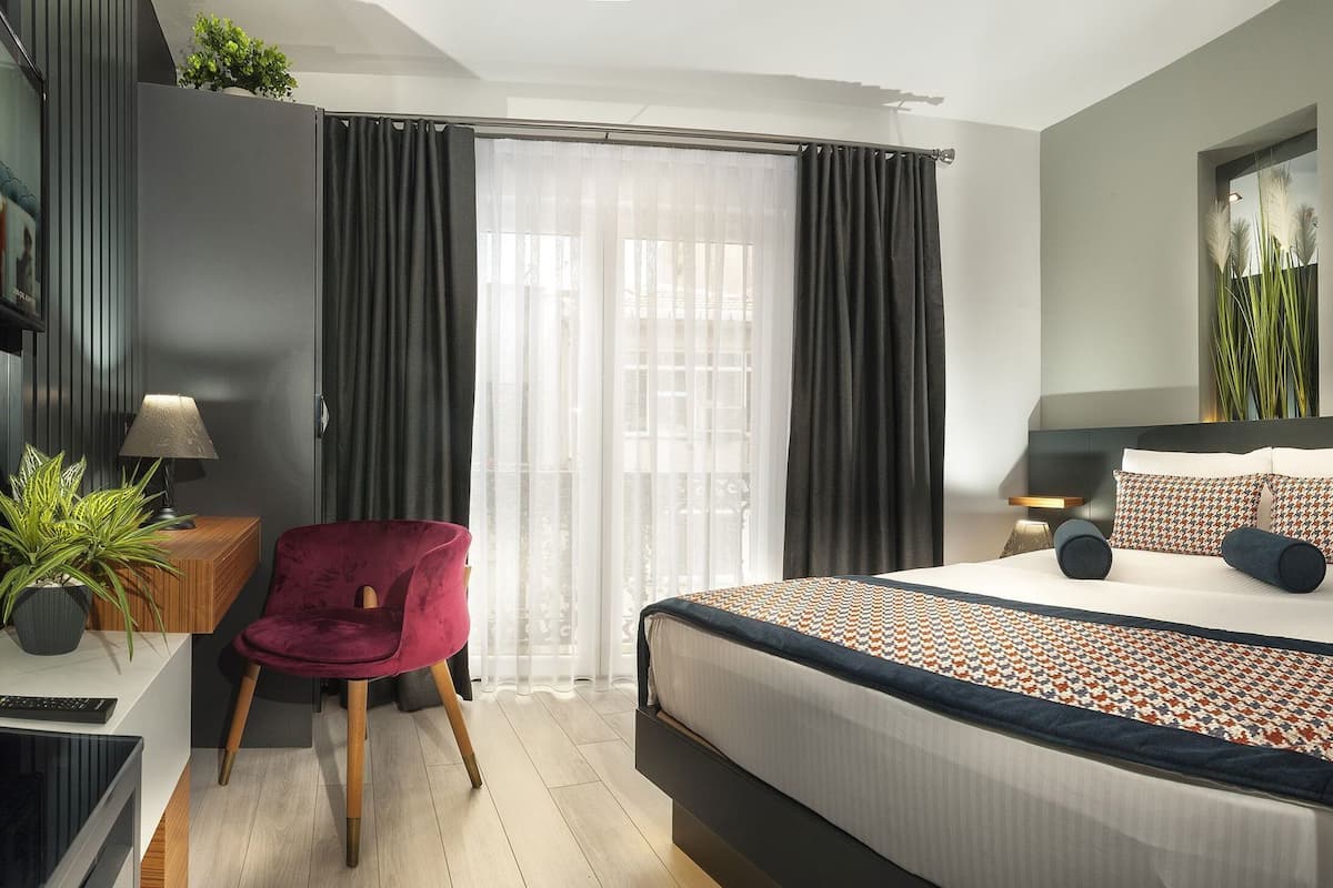 A modern hotel room with a bed, a desk, a chair, and a TV.