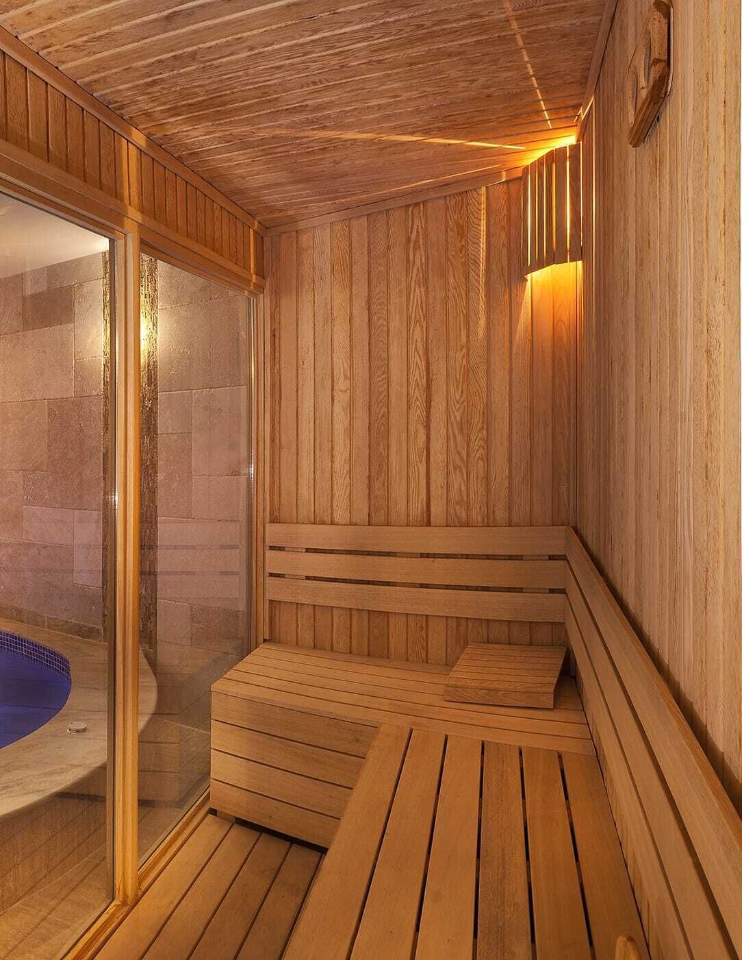 A sauna room with wooden walls and benches, a glass door leading to a pool, and a wall-mounted light fixture.
