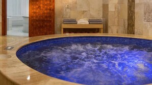 A hot tub with a blue mosaic tile interior, a wooden bench with towels, and a stone wall. - Ooda Rooms Kadıköy (Istanbul)