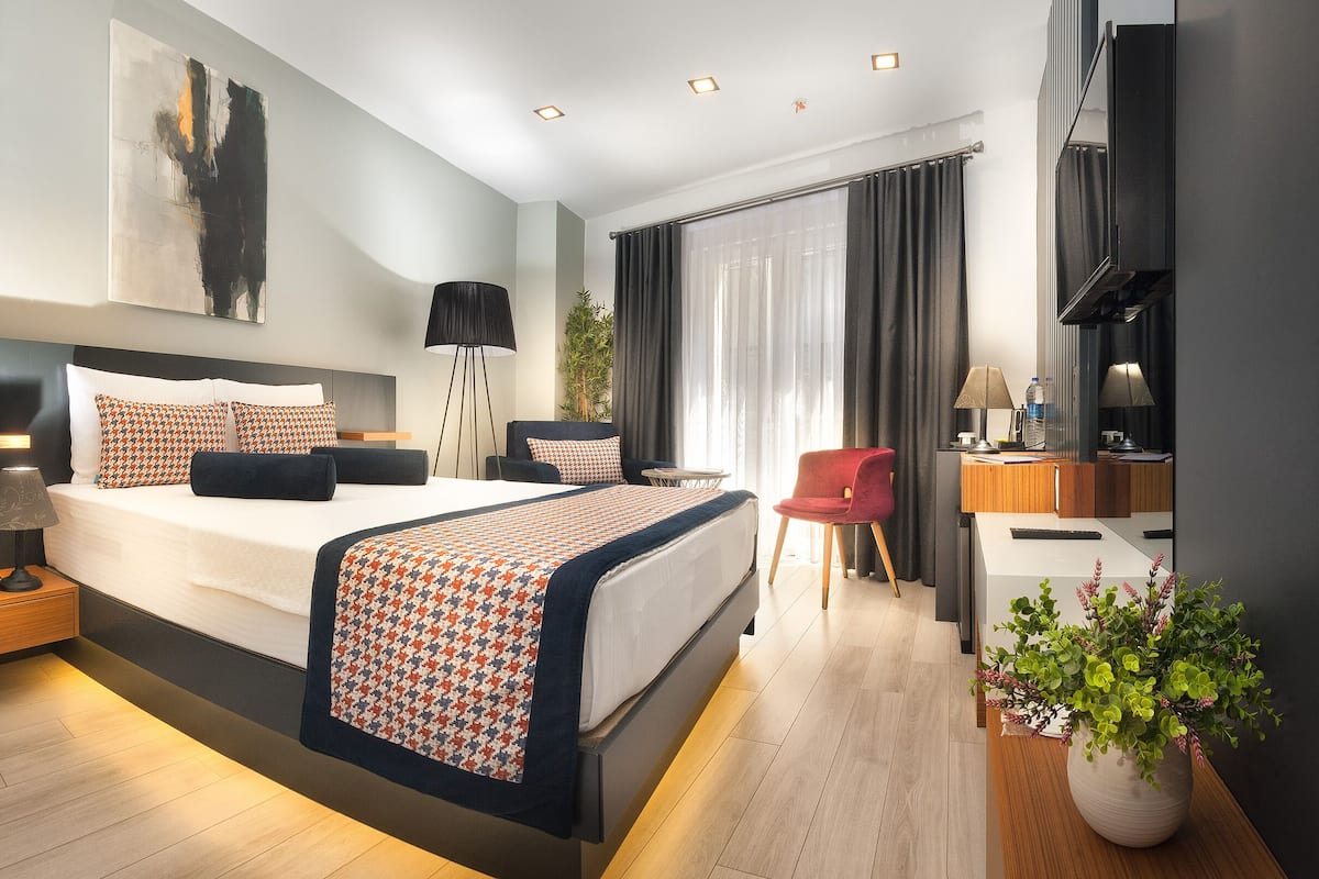 A modern hotel room with a large bed, bedside tables, a desk, and a potted plant.