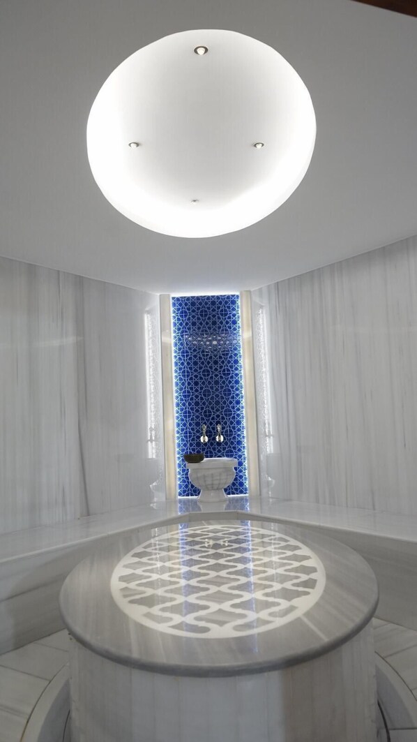 Un baño moderno con tocador de mármol redondo, pared con diseño azul y lámpara de techo blanca.