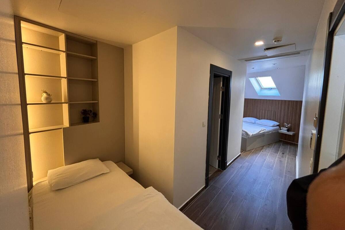 A compact hotel room with a bed, a built-in shelf unit, a skylight, and a small seating area.
