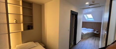 Una habitación de hotel compacta con una cama, una estantería empotrada, un tragaluz y una pequeña zona de estar.