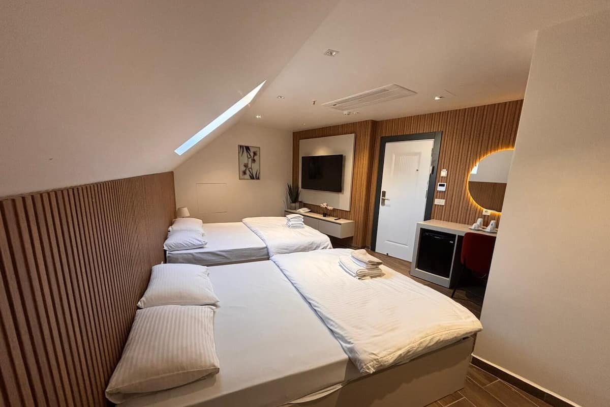 A hotel room with two beds, a TV, a desk, a mirror, and a small kitchenette.