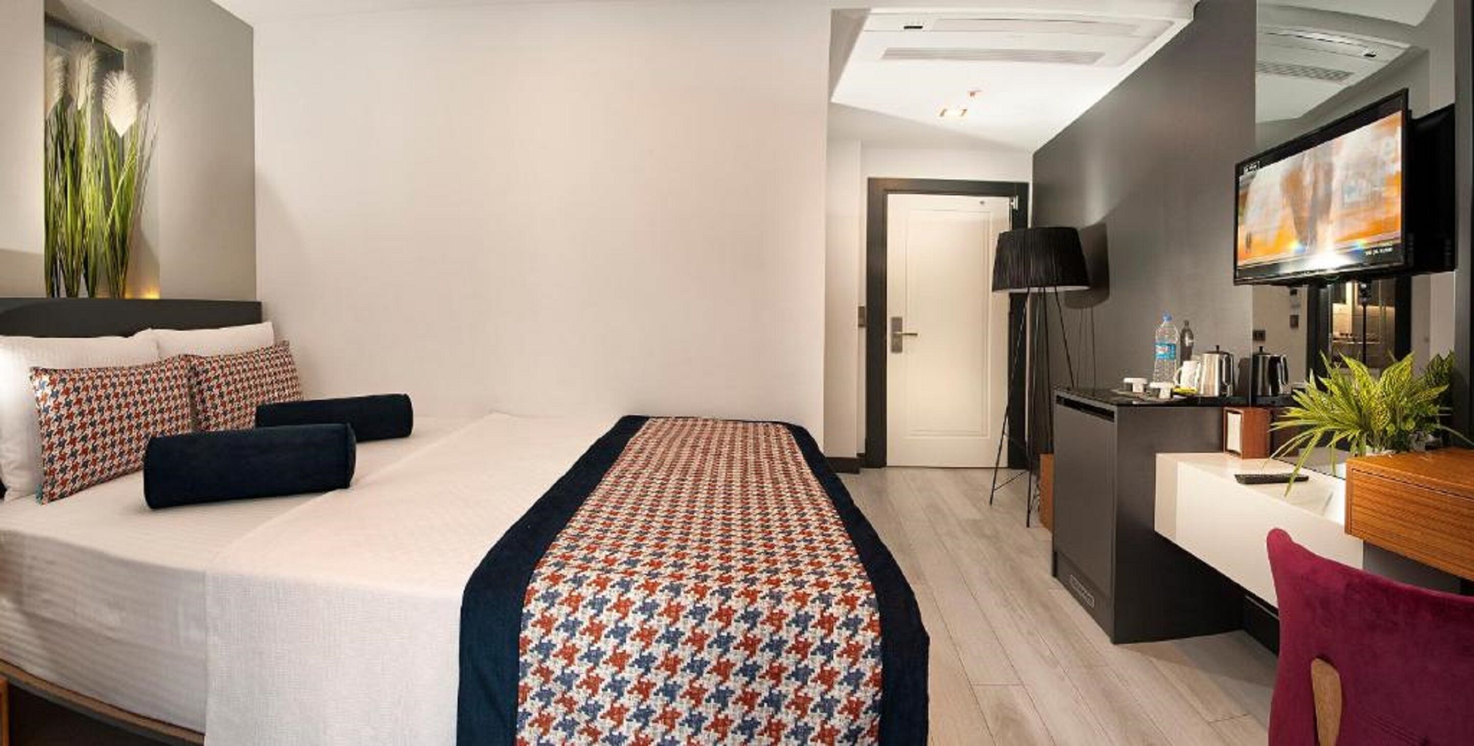 A modern hotel room with a neatly made bed, a desk with a computer, and a television.