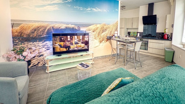 Un salon comprenant un téléviseur, un canapé, un coin cuisine et une grande fresque murale.