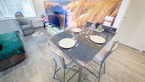 Un coin repas avec une table dressée pour quatre personnes, un téléviseur et une vue sur de hautes herbes et un bâtiment.