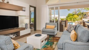 A modern living room with a flat-screen TV, grey sofas, a coffee table, and a view of a pool and greenery outside. - CASA COCO-SUENO Superior 4 Master @ Casa Linda (Sosua)