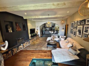 Een moderne woonkamer met een open haard, een bank, een salontafel en een eethoek in de achtergrond.