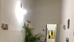 A narrow hallway with a sofa and a potted plant on one side, leading to a room with a yellow wall. - Casa do Meio Pousada (Recife)
