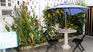 A small outdoor seating area with a round table and two chairs, surrounded by lush greenery and a blue umbrella. - Casa do Meio Pousada (Recife)