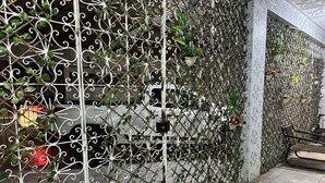 A metal gate with decorative patterns and greenery, a tiled wall with a geometric design, and a bench. - Casa do Meio Pousada (Recife)