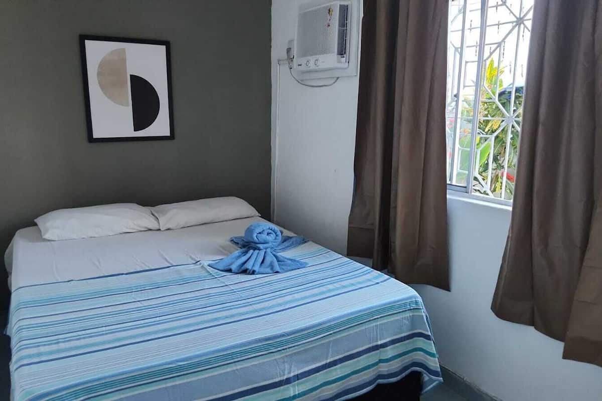 Habitación de hotel con cama, una obra de arte enmarco, un equipo de aire acondicionado y una ventana con cortinas.