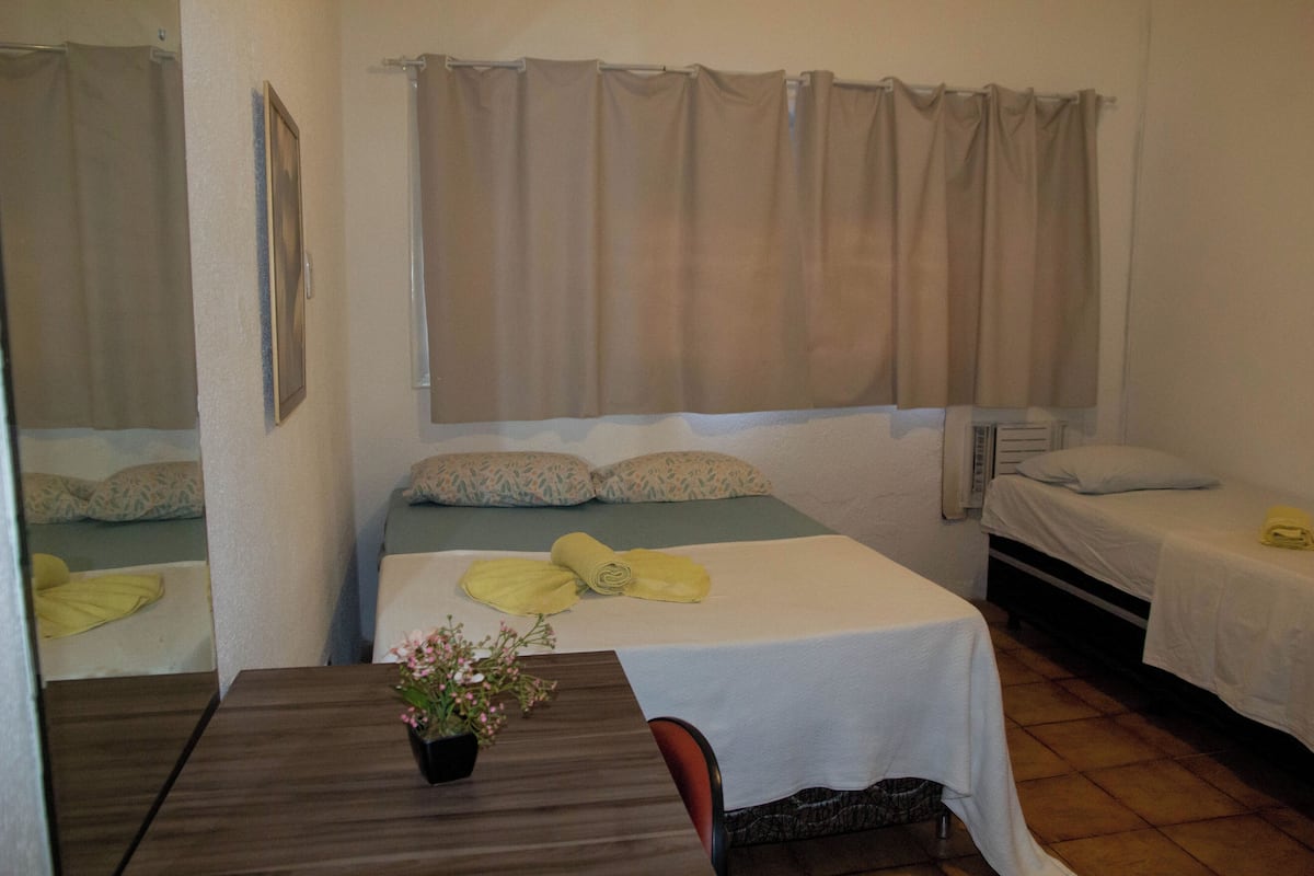 Una habitación de hotel con dos camas, una mesa con un jarrón de flores y una ventana con cortinas.