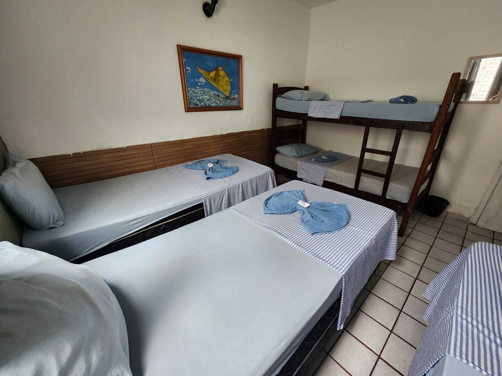 A room with two single beds, a bunk bed, a wooden headboard, a framed picture on the wall, and a tiled floor.