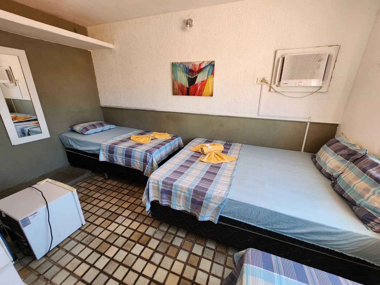 Une petite chambre d’hôtel, de taille modeste, avec deux lits simples, une petite kitchenette, un miroir et une peinture abstraite aux couleurs vives accrochée au mur.