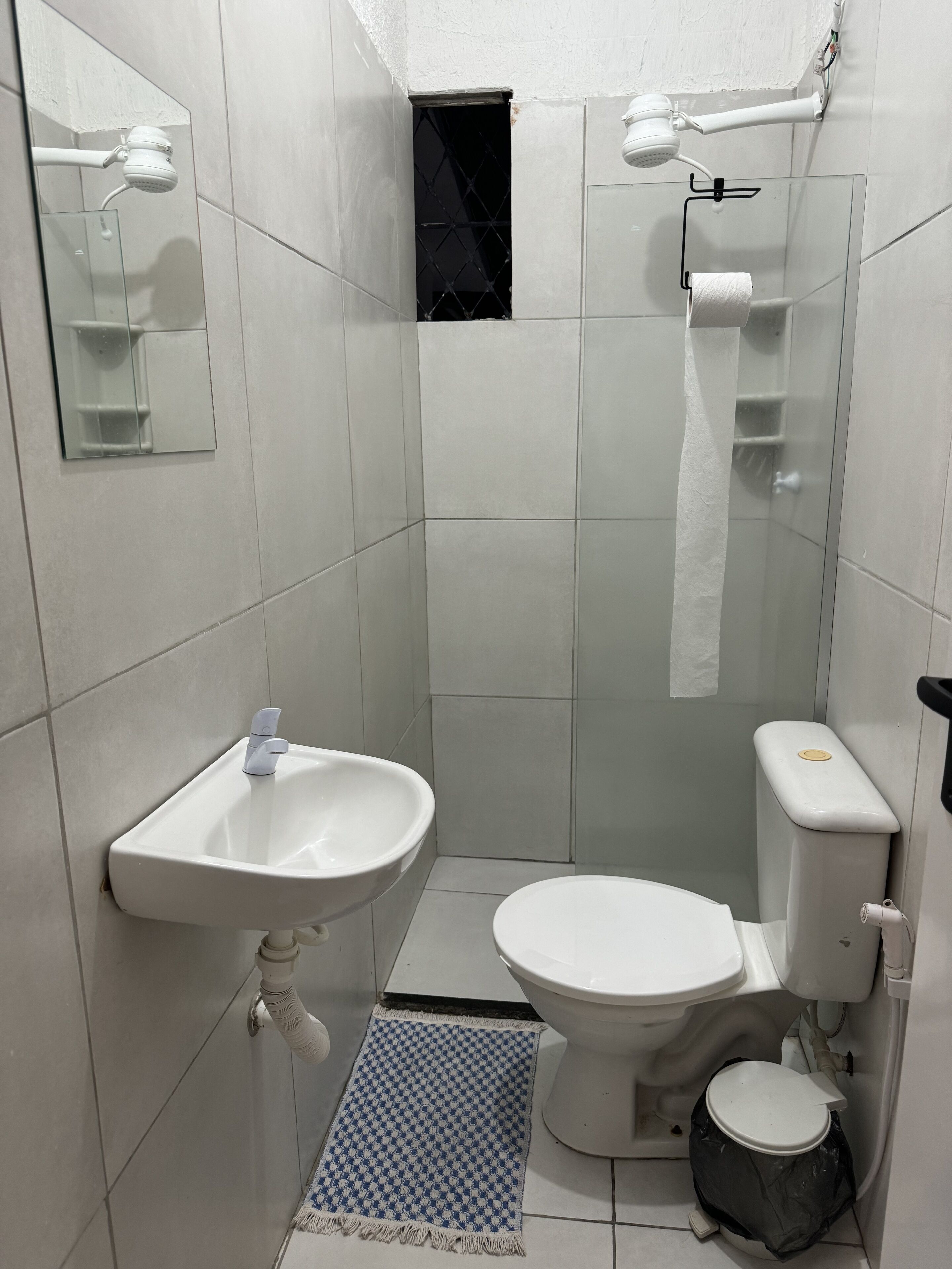 Casa de banho pequena e limpa, com lavatório, sanita e chuveiro brancos.