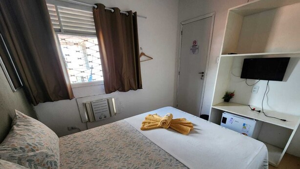 A hotel room with a bed, a desk with a computer, a TV, and a window with curtains. - Casa do Meio Pousada (Recife)