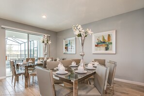 A dining area with a glass table, chairs, and white teapots. There are two vases with flowers on the table. - Fantastic 10 Bed Game Spa Pool Home at Sonoma Resort (Kissimmee)