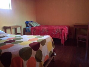 A room with a bed covered in a colorful polka dot bedspread, a bedside table, a chair, and a small table with a red cloth. - Casa Refugio House (Cusco)