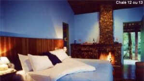 A bedroom with a large bed, a stone fireplace, and a view of the outdoors. - Pousada no Caminho do Marimbondo (Itatiaia)