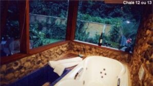 A bathroom with a stone wall, a bathtub, and a view of a garden. - Pousada no Caminho do Marimbondo (Itatiaia)